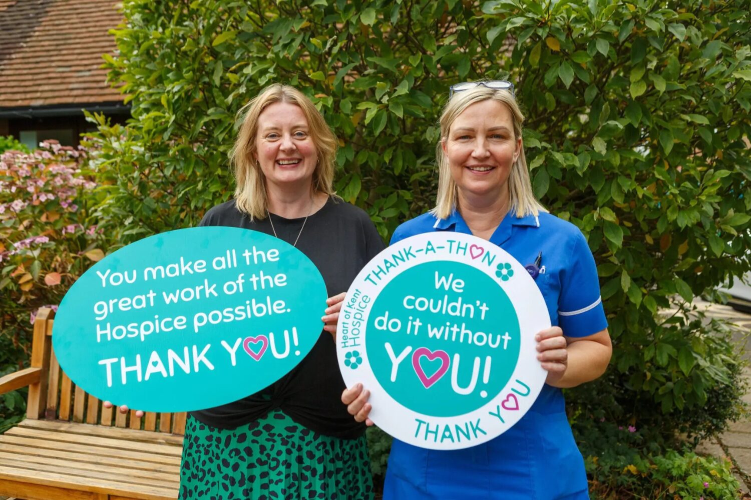 Thankathon Two ladies standing in the hospice garden holding 'thank-a-thon' signs